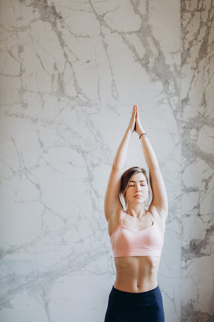 Young woman performing upward salute yoga pose indoors with marble background.